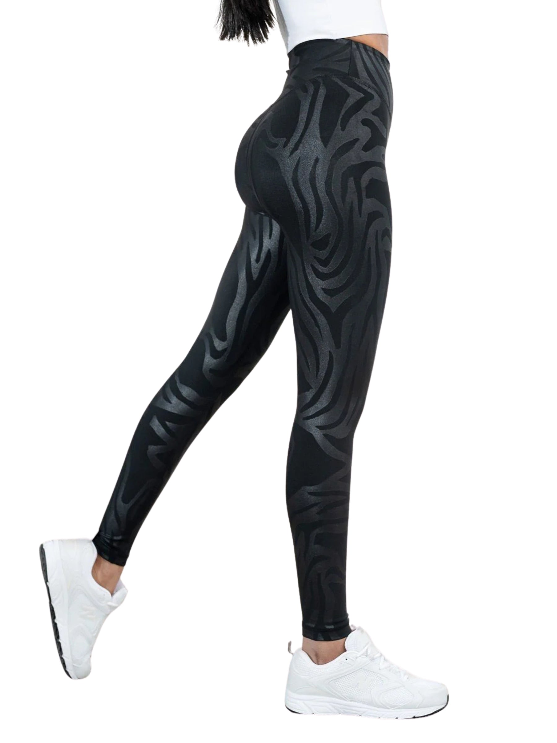 Model Lismina in Leggings 468 Lanzarote in Lederoptik in Schwarz und weißen Sneakers, seitlich stehend, ein Bein angehoben.